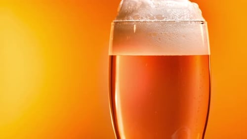 Refreshing Beer with Frothy Head on Orange Background