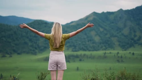 Graceful Woman Hiker with Raised Hands Enjoys Green Valley