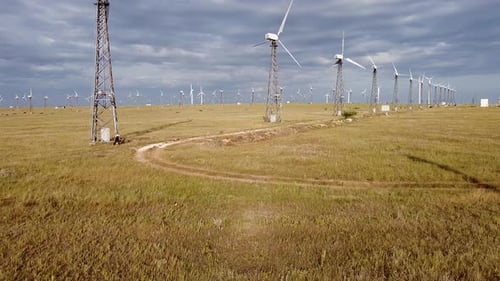 Una vista aérea de un Zumbido volando cerca de turbinas eólicas blancas a mediana altitud de pie en una estepa