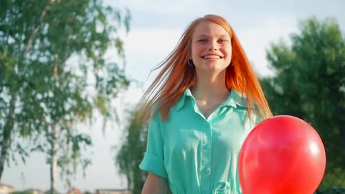 Red-haired Woman with Balloons Walking in a Park