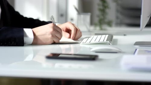 Hands of Businessman Writing in Notepad at Office Desk