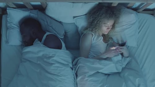 Woman Using Phone while Husband Sleeping