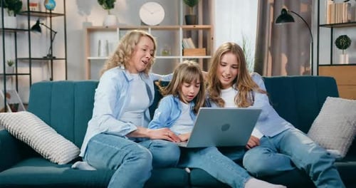 Personas femeninas que descansan en un sofá suave en casa y revisan un interesante programa en una computadora portátil