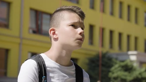 A Caucasian Teenage Boy Looks Around Closeup a School in the Background