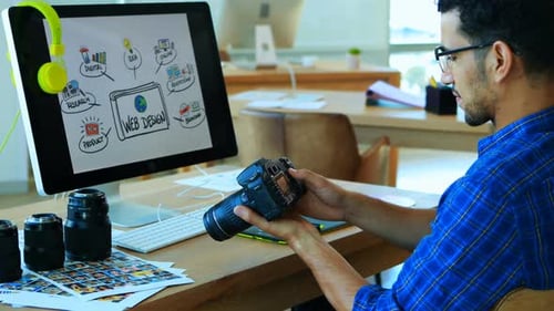 Man Inspects Camera at Desk with Web Design