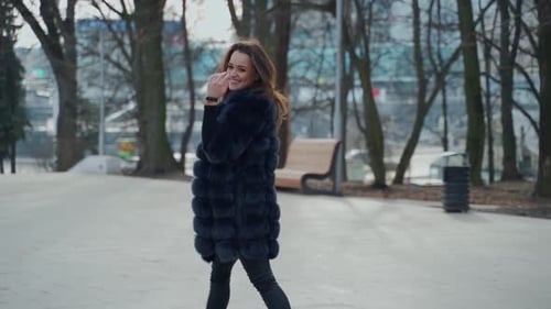 Happy model walking. Beautiful young woman in stylish fur coat walks in the park.