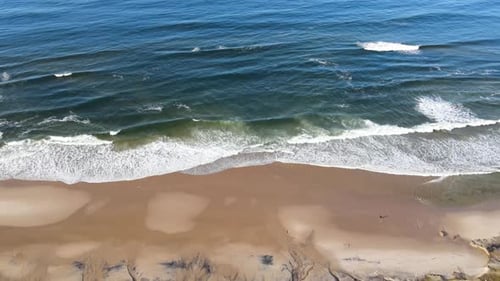 Flying over a beach, across the waves towards the ocean (aerial view)