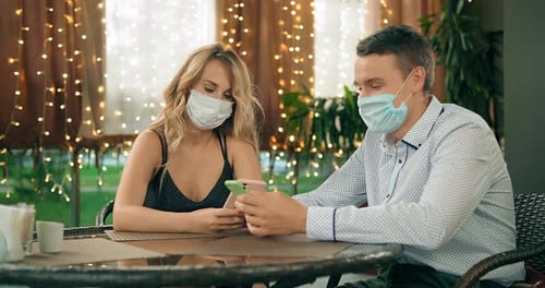 Couple at Table Wearing Masks Using Smartphone