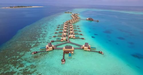 Aerial drone view of scenic tropical island and resort hotel with overwater bungalows in Maldives.