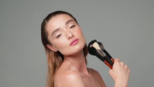 Woman Posing with Makeup Brushes in Studio