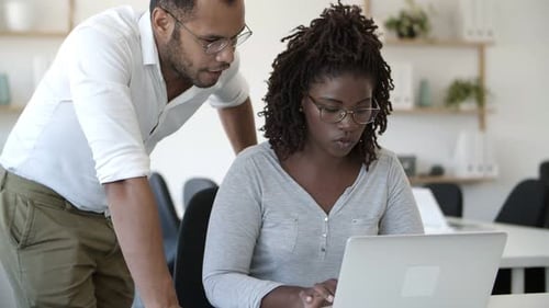 Man Assisting Woman Using Laptop in Office