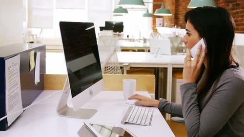 Woman Talking on Phone and Typing at Desk