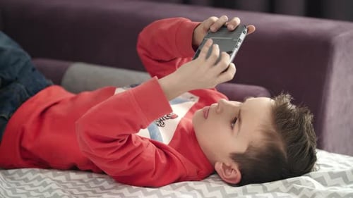 Boy Lying on Bed Playing with Smartphone