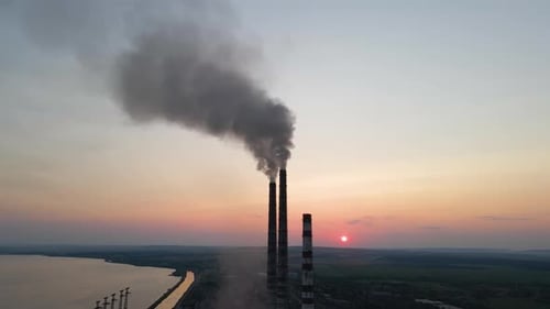Luftaufnahme der hohen Rohre eines Kohlekraftwerks mit schwarzem Rauch, der sich nach oben bewegt und die verschmutzende Atmosphäre bei