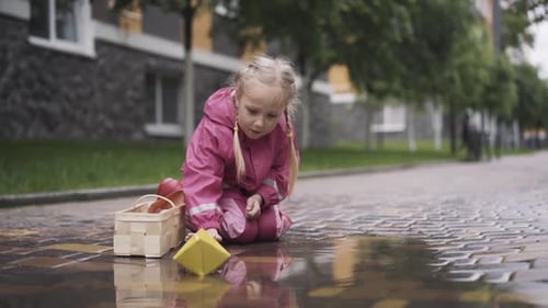 Girl Plays with Paper Boat in Urban Puddle