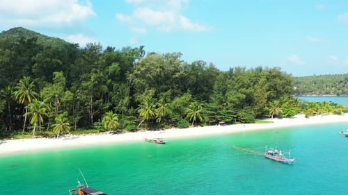 Peaceful exotic beach with palm trees over white sand, calm turquoise lagoon with anchored boats for