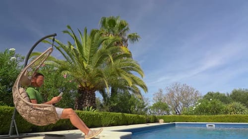Man Relaxing in Hanging Chair by Tropical Pool