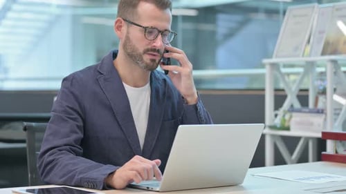Man Talking on Phone and Using Laptop in Office
