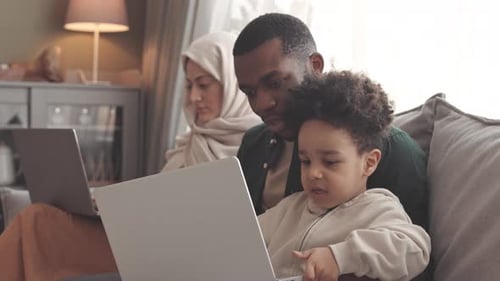 Modern Interracial Family of Three Sitting on Sofa with Laptops