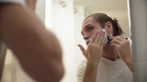 Homem raspando barba com navalha no banheiro