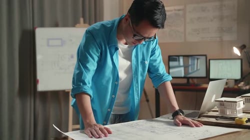 Asian Man Engineer With A Laptop Looking At Blueprint While Working At The Office