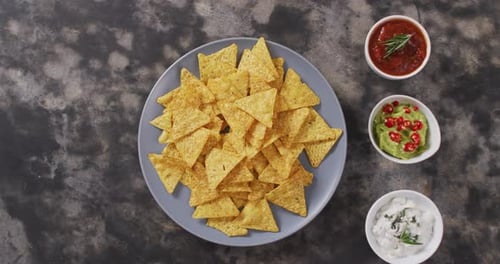 Primer plano de nachos en un plato y salsas sobre una superficie negra