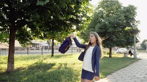 Schoolgirl waving backpack runs down the alley