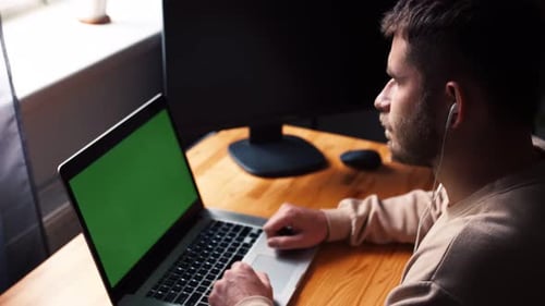Young Caucasian Man at Home Office Sits Table Communicates Talk Speak with Green Screen Laptop
