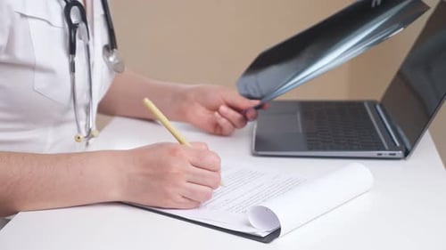 Doctor Works with Xray Picture and Papers on Clipboard at Table in Office