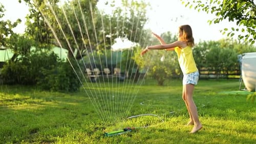 Happy kid girl jouant avec arroseur de jardin courir et sauter