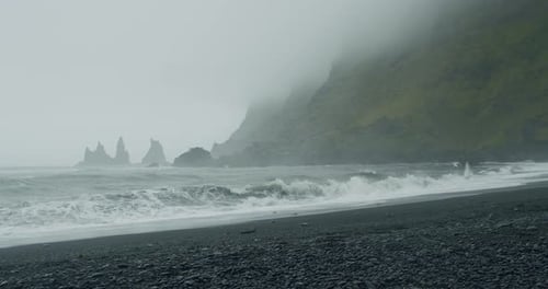 The Black Sand Beach of Reynisfjara with Waves Hitting the Shore on Foggy Rainy Stormy Day