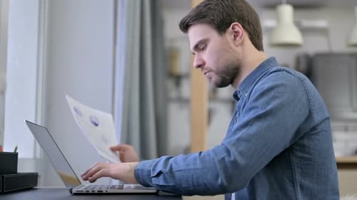 Beard Junger Mann gibt Daten von Dokumenten auf Laptop ein