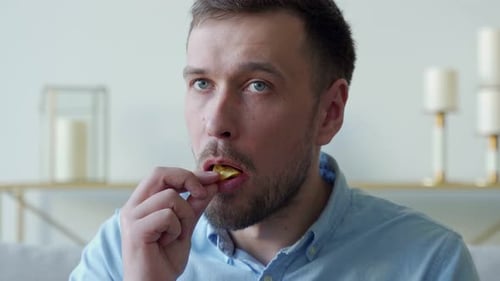 Man Sits on the Couch and Eats Potato Chips