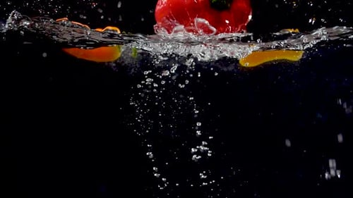 Lebendige Paprika, die in Zeitlupe ins Wasser fällt.