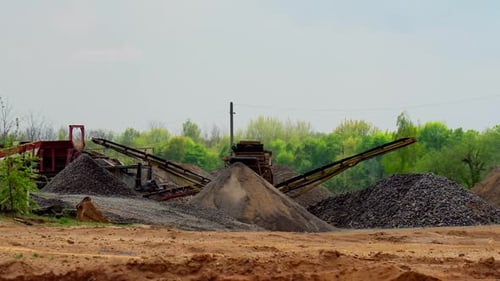 Construction works. Piles of stones on the ground and industrial machine on green nature background.