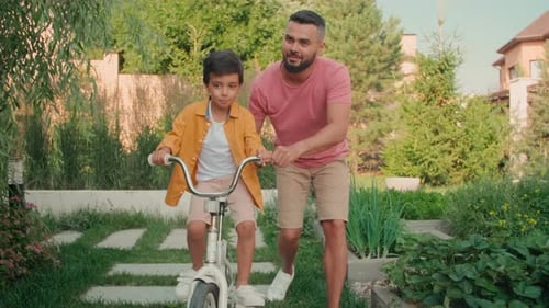Father Teaching Son to Ride Bike in Yard