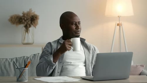 Afrikanischer Mann am Laptop trinkt Kaffee und arbeitet zu Hause