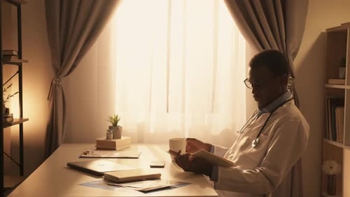 Doctor Reading Book with Coffee in Office