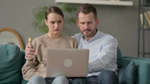 Worried Couple Using Laptop at Home on Sofa