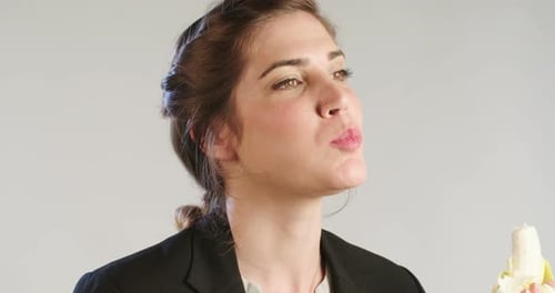 Close up of a woman eating a banana on a white studio background