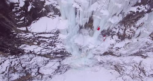 Drohnenaufnahme eines Mannes, der auf einem gefrorenen Wasserfall in den Bergen eisklettert