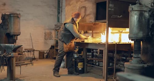 Man Works with Fiery Metal at a Forge