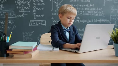 Zeitlupe eines intelligenten Kindes, das Laptop benutzt und dann am Schreibtisch im Klassenzimmer der Universität schreibt