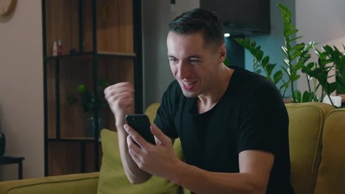 Excited man looking at mobile phone screen indoors