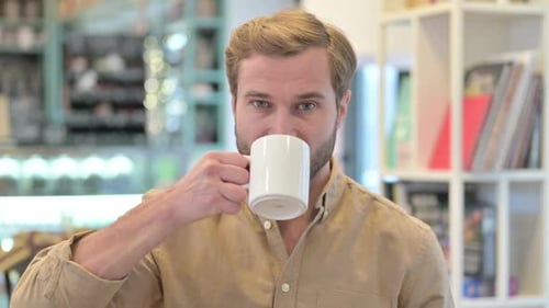 Porträt eines schönen jungen Mannes beim Kaffeetrinken