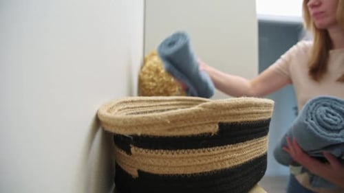 Woman Placing Blue Rolled Towels in Basket