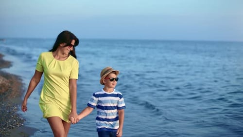 Happy Mother and Son Walking on Sea Beach Together at Sunset