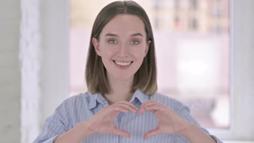 Young Woman Makes Heart Shape with Hands Smiling