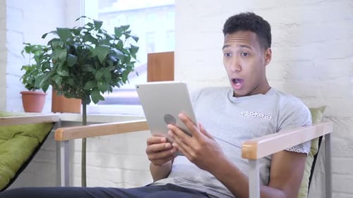 Surprised Young Adult Looking at Tablet Indoors