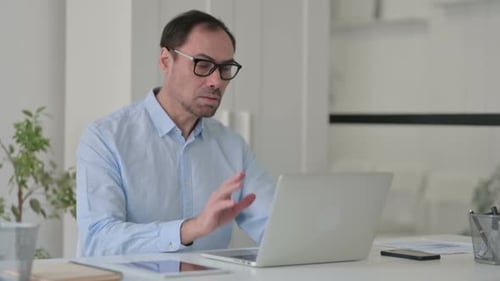 Middle Aged Man Talking on Video Call on Laptop in Office
